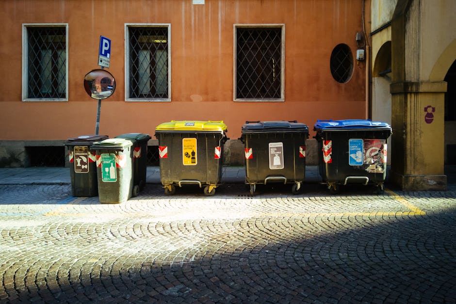 pexels-photo-4124936-4124936 Five recycling bins on a sunny cobblestone street against an orange building.